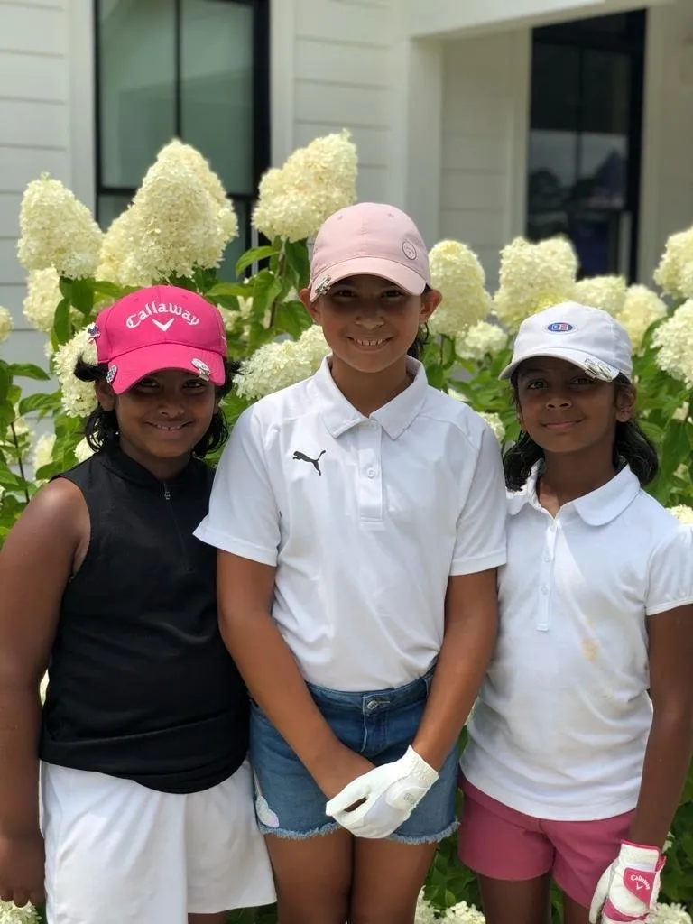 Three girls are posing for a picture in front of some flowers.