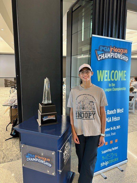 Young person posing next to a championship trophy and welcome banner.