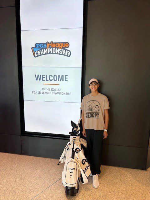 Person standing next to a golf bag in front of a large welcome sign for a golf championship.